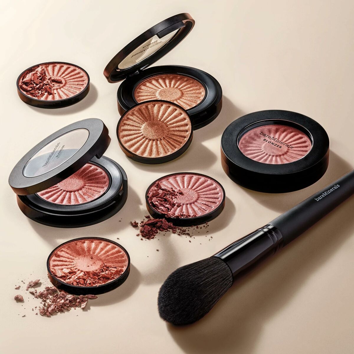 bareMinerals makeup products and brush arranged aesthetically on a beige surface.