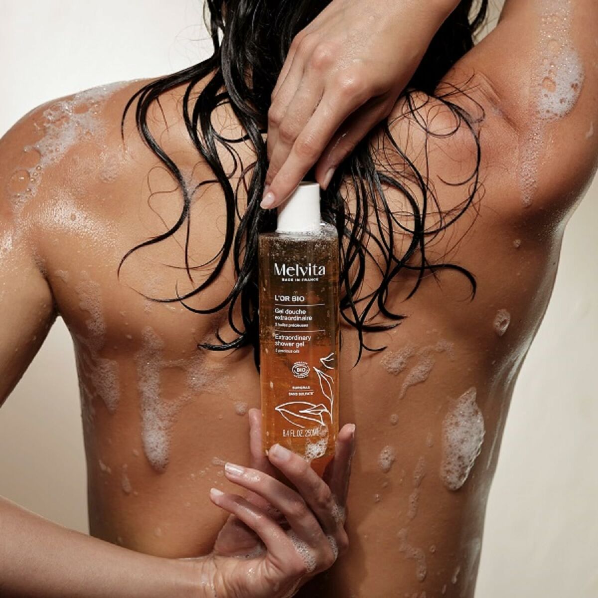 Mousse nettoyante Melvita L'OR BIO 250 ml with a person applying it in the shower, showcasing natural ingredients and a luxurious texture.