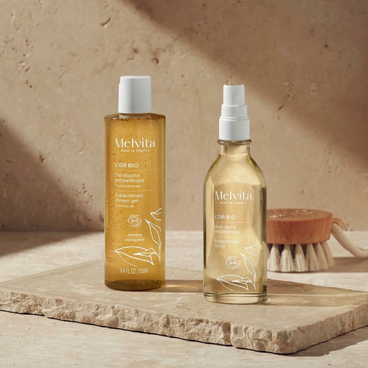 Melvita L'OR BIO cleansing mousse and oil on a stone surface, showcasing natural skincare products for all skin types.