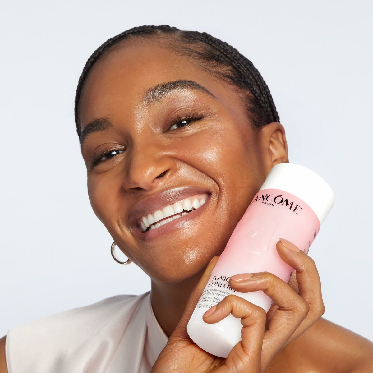 Femme souriante tenant le gel nettoyant visage Lancôme CONFORT 400 ml, produit de beauté pour peau sèche.