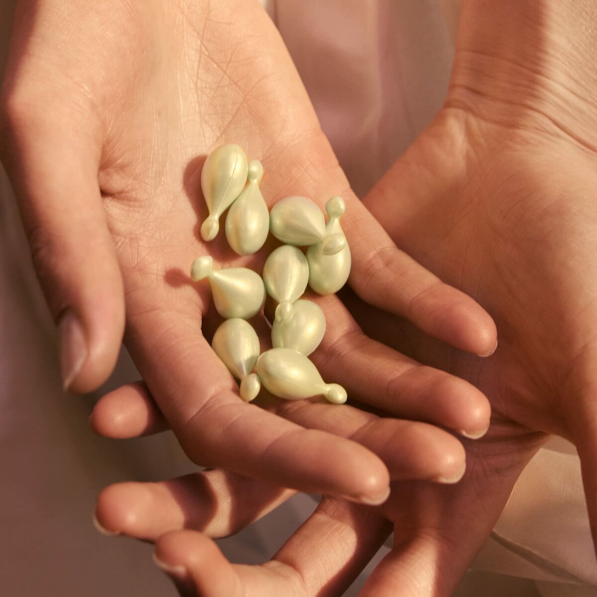 Hands holding green capsules of Eve Lom facial oil, highlighting skincare and beauty care