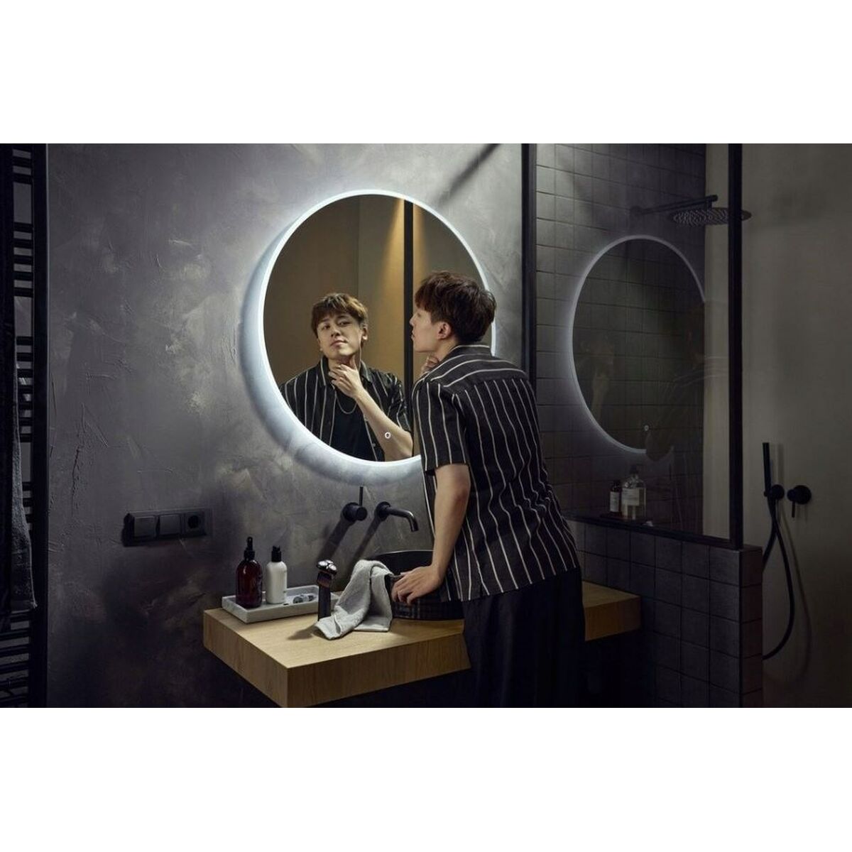 Person grooming in modern bathroom with circular mirror, showcasing a stylish and sleek interior.