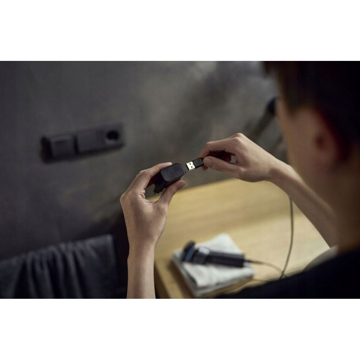 Person connecting USB charger for Philips X5006/00 electric razor on a wooden surface.